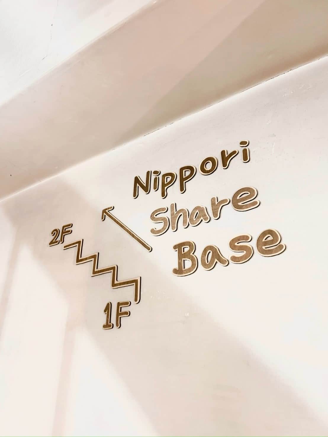 階段の壁に付けられた木製の案内サイン。1Fから2Fの Nippori Share Base への矢印